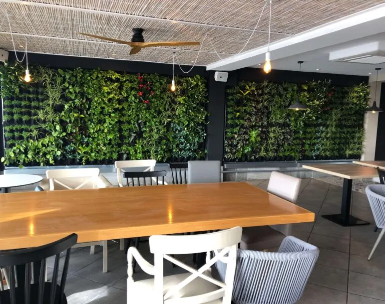 Interior de restaurante moderno con paredes de jardín vertical, mesas de madera y sillas de diseño.