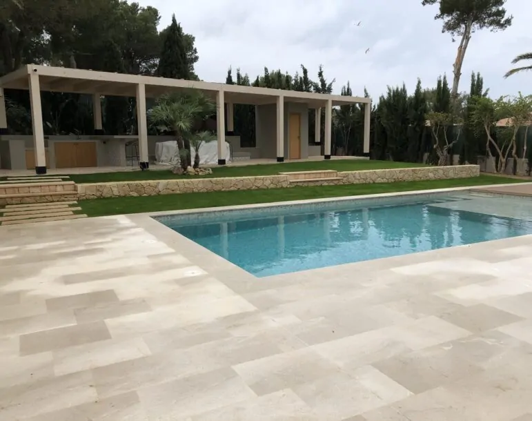 Piscina de agua cristalina con terraza de piedra y pérgola moderna en un jardín rodeado de vegetación