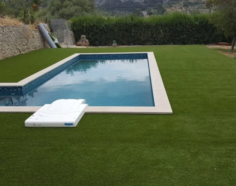 Piscina rectangular con agua cristalina rodeada de césped en un jardín con vistas a la montaña.