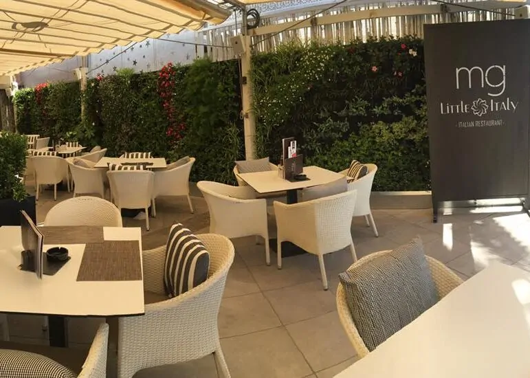 Terraza de restaurante con jardín vertical, mesas elegantes y sillas de mimbre bajo pérgola