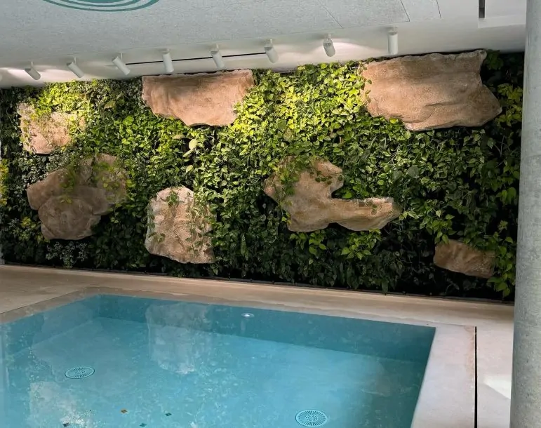 Piscina interior con agua cristalina junto a un jardín vertical con rocas decorativas y luces LED